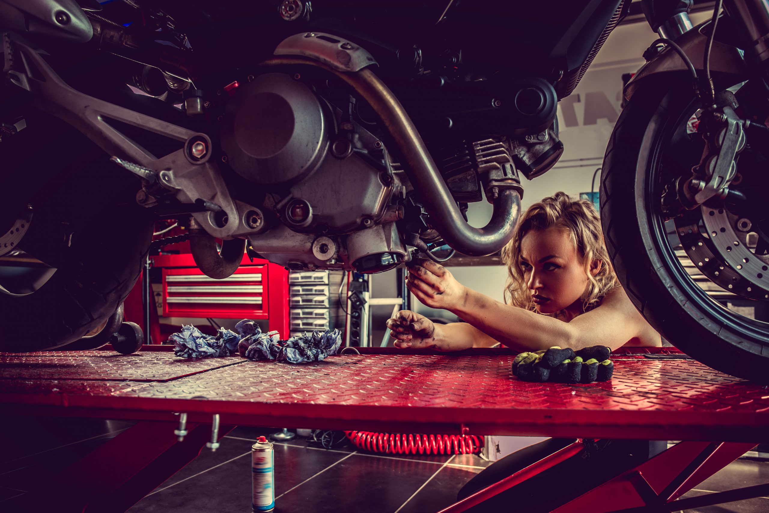 Blond female mechanic repairing motocycle engine. Close up image